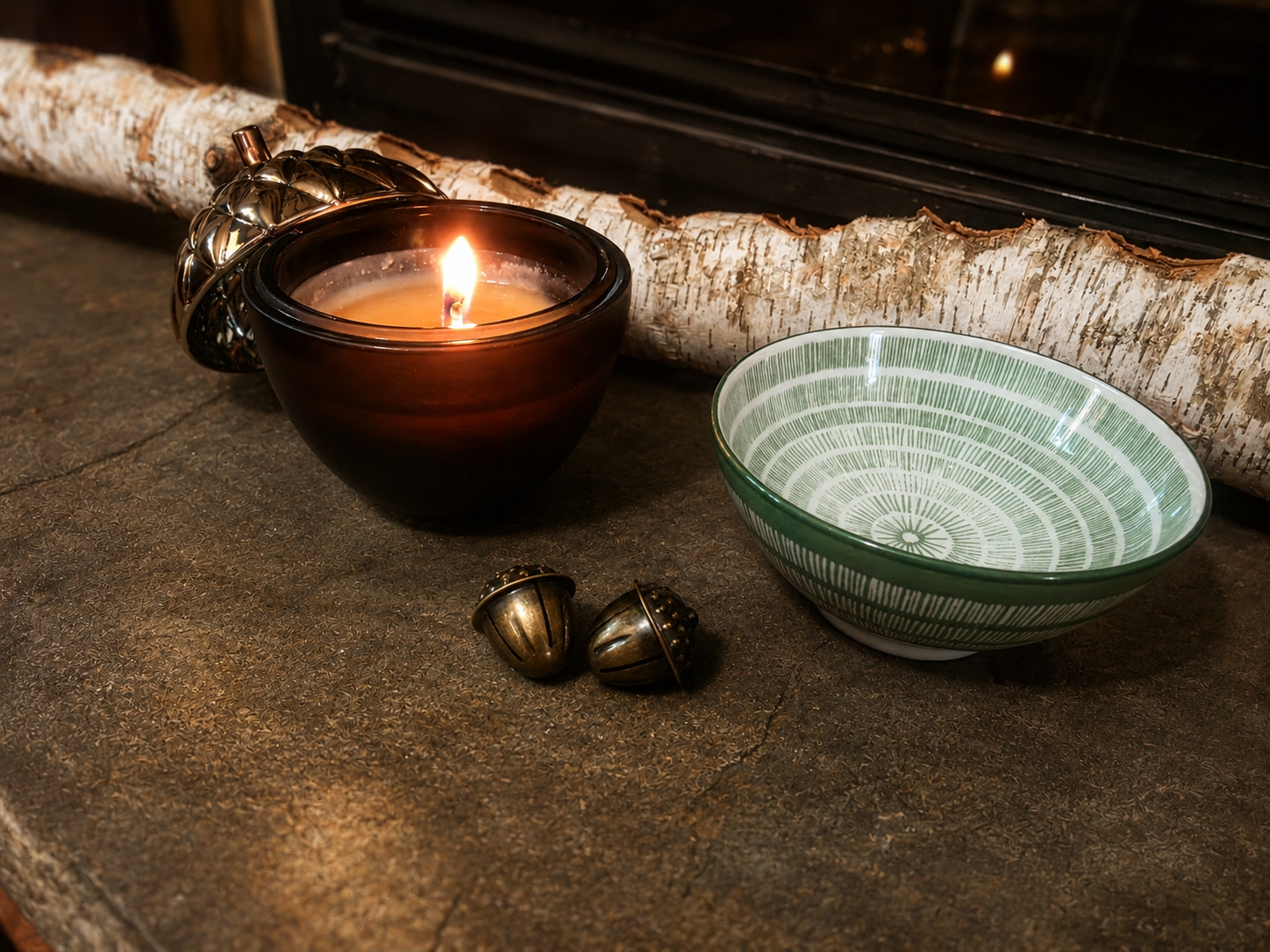 A lit candle, patterned bowl of water, metal acorns, and a birch branch prepared for the acorn charm ritual.