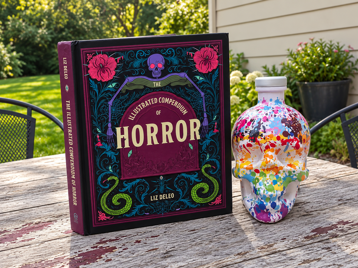 The Illustrated Compendium of Horror beside a colorful skull-shaped bottle on a rustic outdoor table.